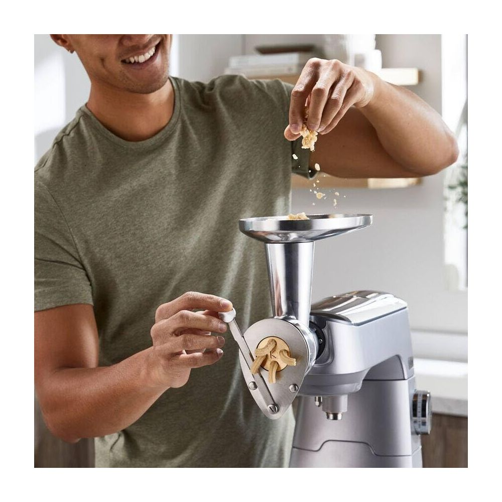 Mężczyzna używa przystawki do maszynki do mięsa, wkłada jedzenie.