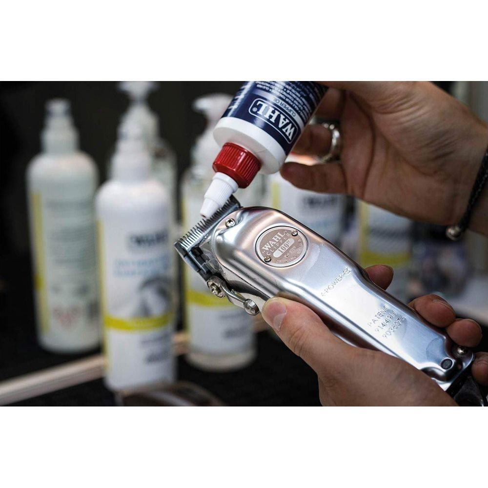 Manos sosteniendo una cortapelos plateada, aplicando aceite en la cuchilla.