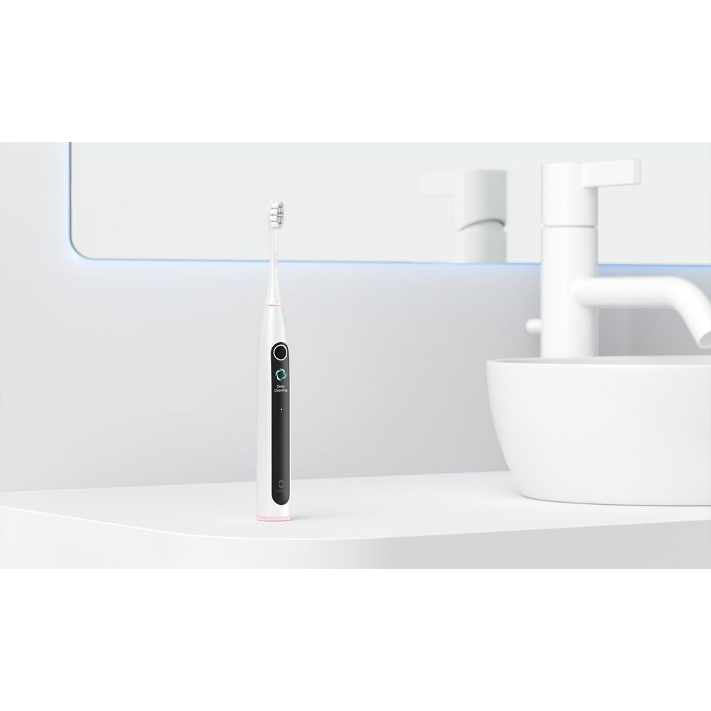 Eine weiße elektrische Zahnbürste mit rosa Akzenten steht auf einem weißen Regal neben einem Waschbecken.