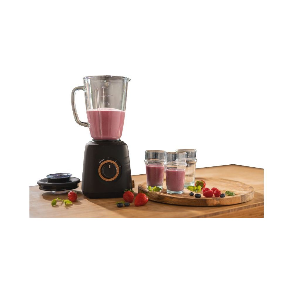 Ein schwarzer Mixer mit Fruchtshake steht auf einem Holztisch, daneben Gläser mit Shake.