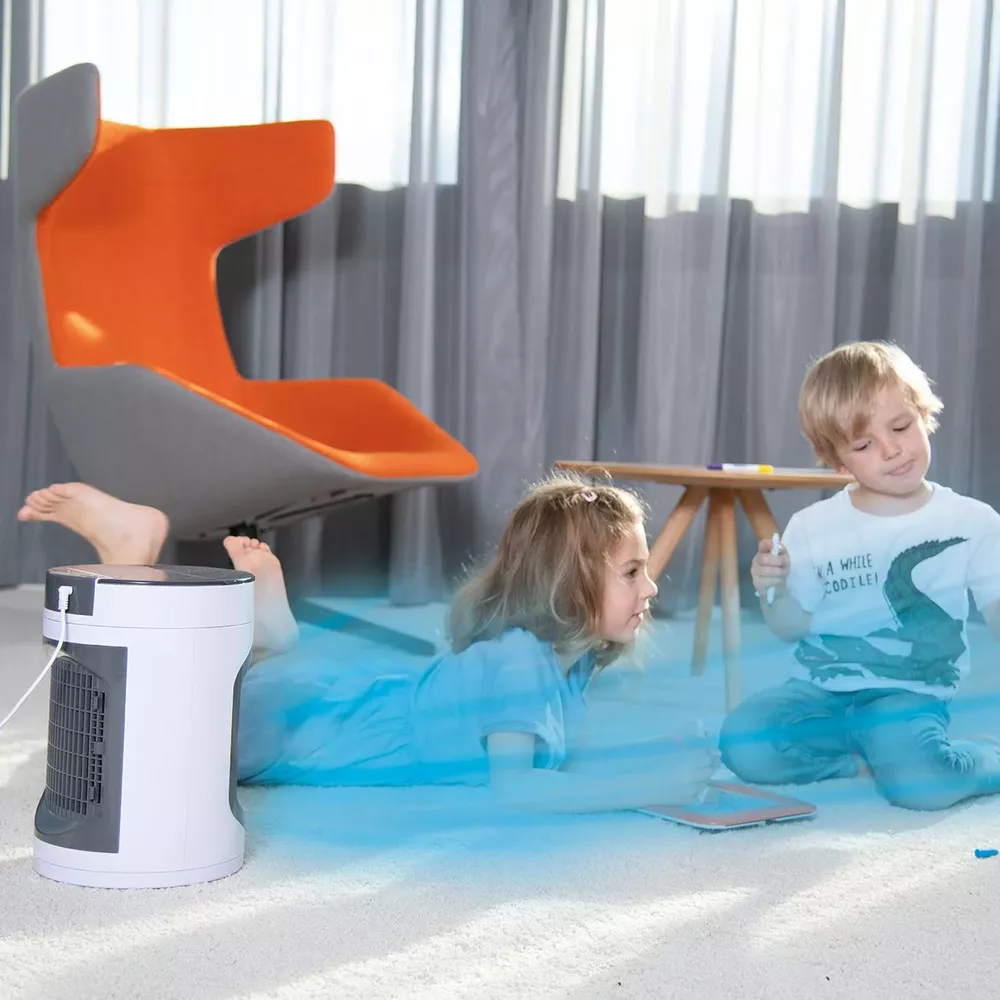 Zwei Kinder liegen auf dem Teppich vor einem orange-grauen Stuhl und einem Tisch. Ein Luftkühler steht links.
