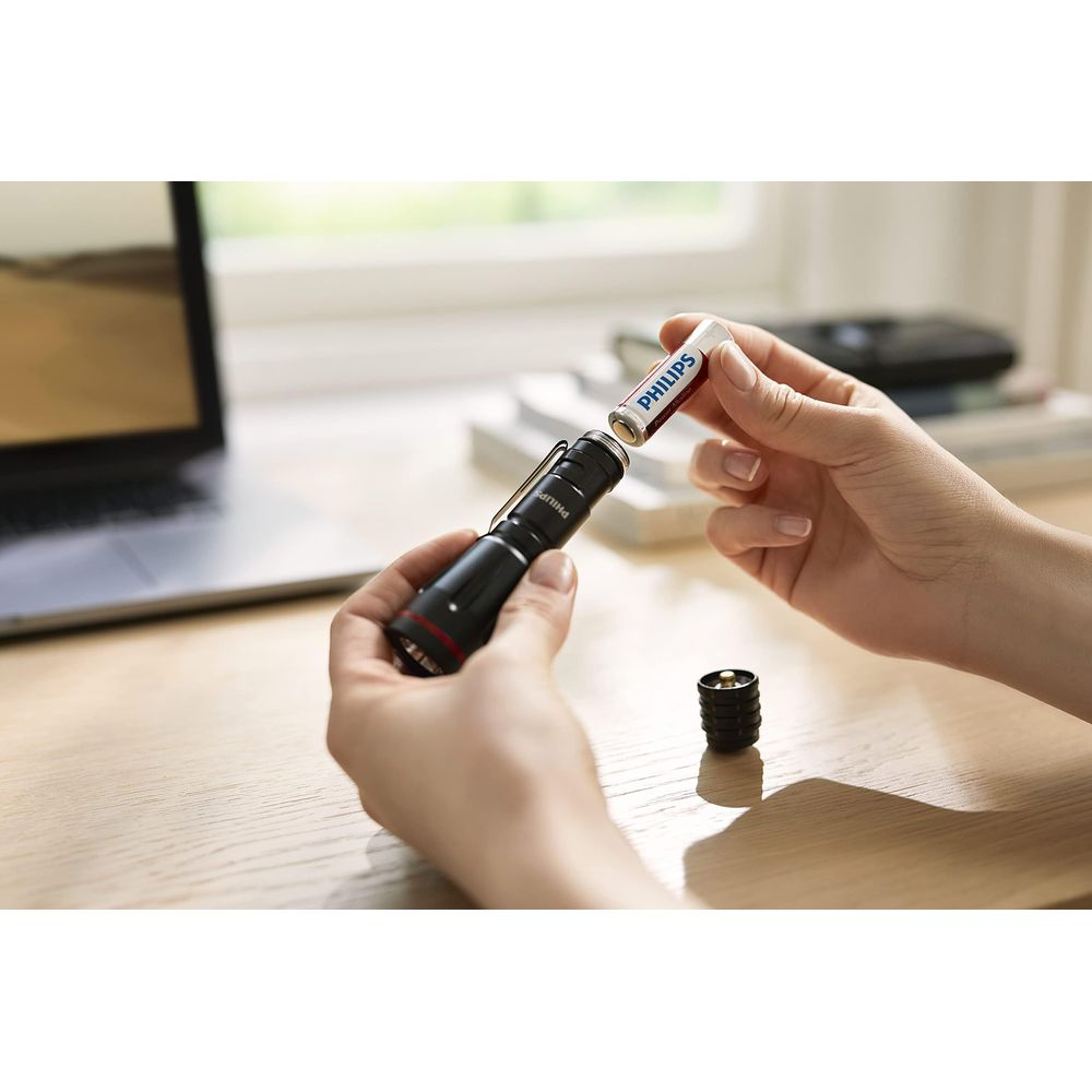 Una mano inserisce una batteria Philips in una torcia nera.