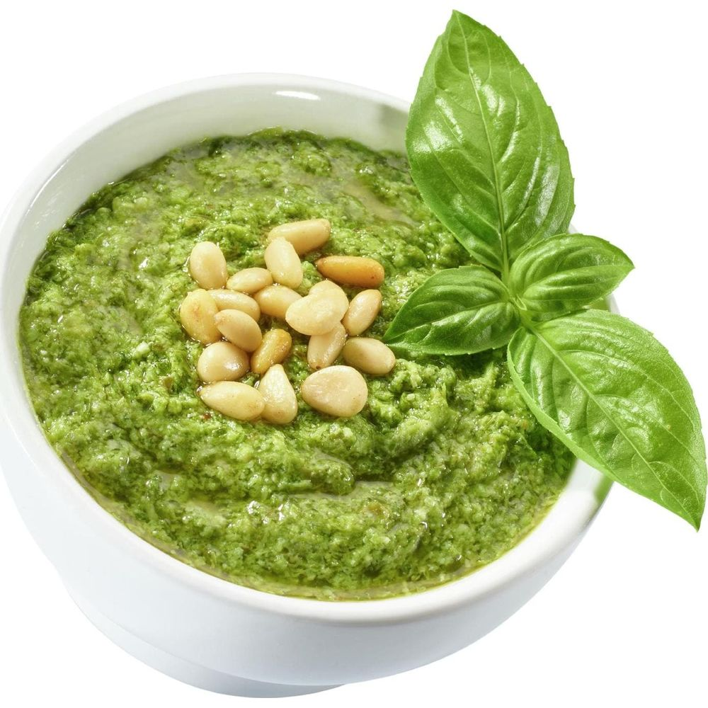 Zielone pesto w białej misce, udekorowane orzeszkami pinii i bazylią.