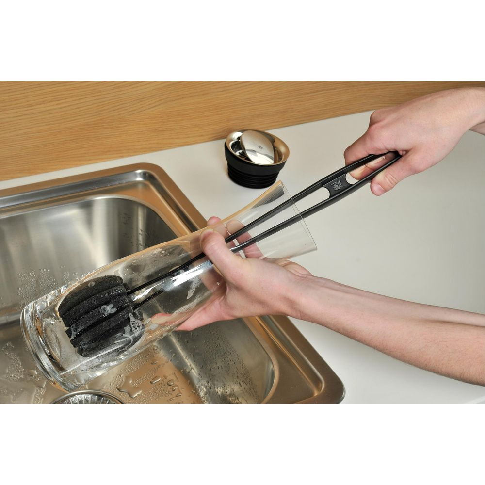 Bir kişi lavaboda bir fırça ile bardak temizliyor.