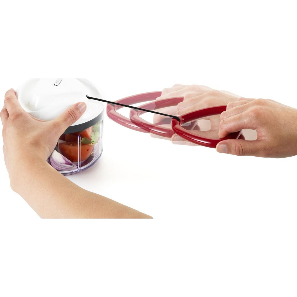 Mani che usano un tritatutto con manico rosso e verdure.