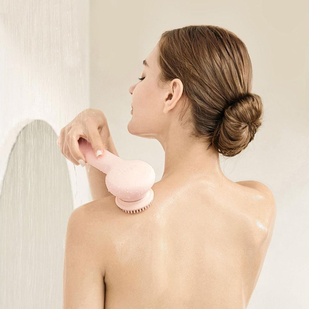Una donna con i capelli raccolti usa una spazzola rosa mentre fa la doccia.