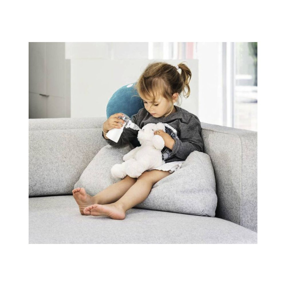 Ein kleines Mädchen füttert einen Teddybären mit einer Spritze auf dem Sofa.