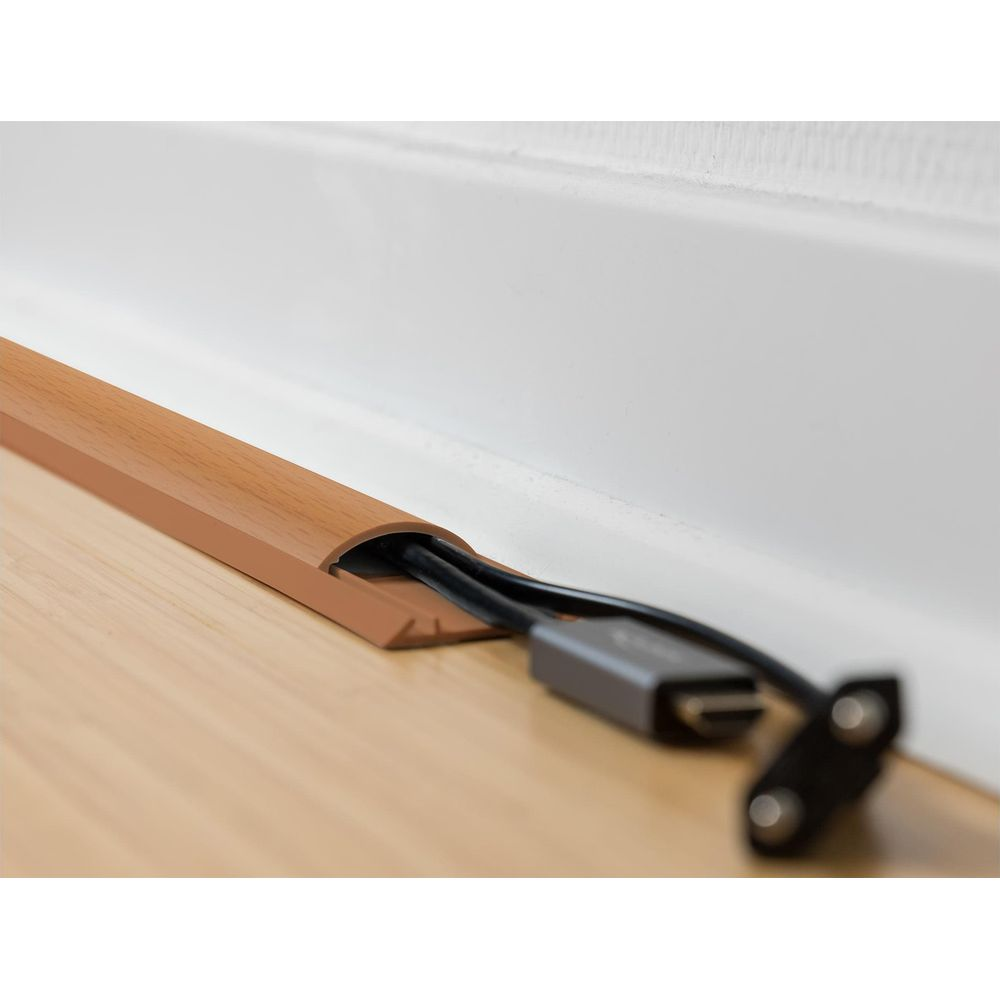 Ein brauner Kabelkanal mit schwarzen Kabeln und einem grauen Adapter liegt auf einem Holzboden.