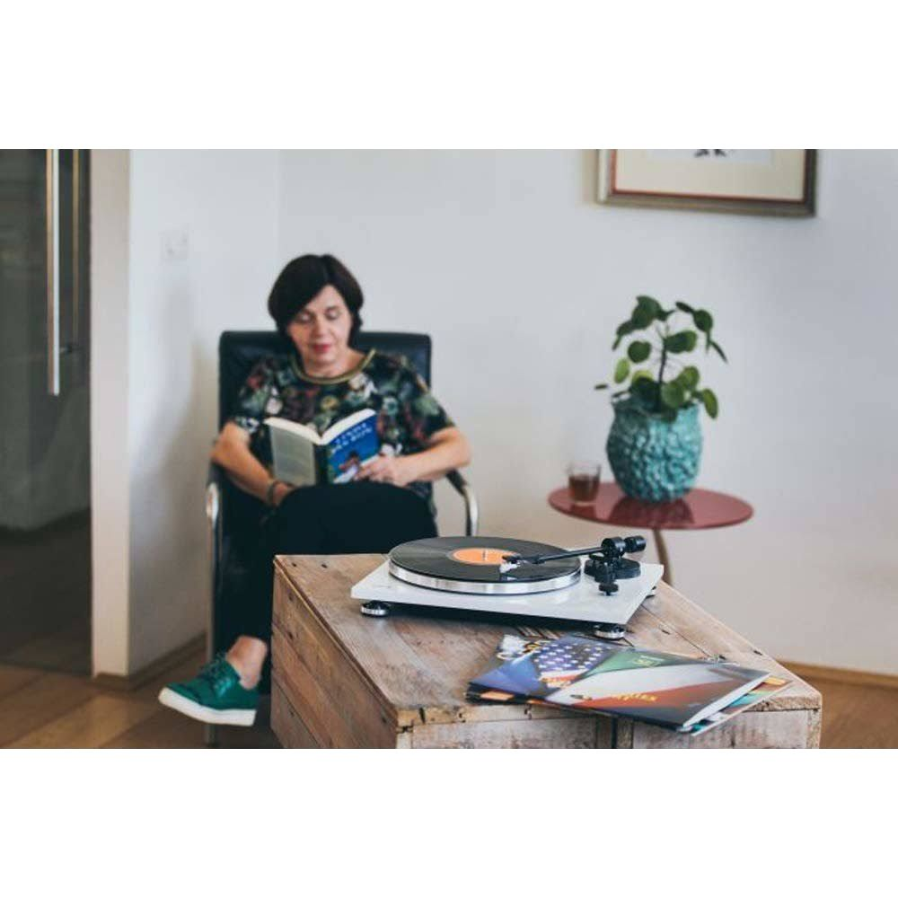 Femme lisant un livre, assise dans un fauteuil à côté d'une platine.