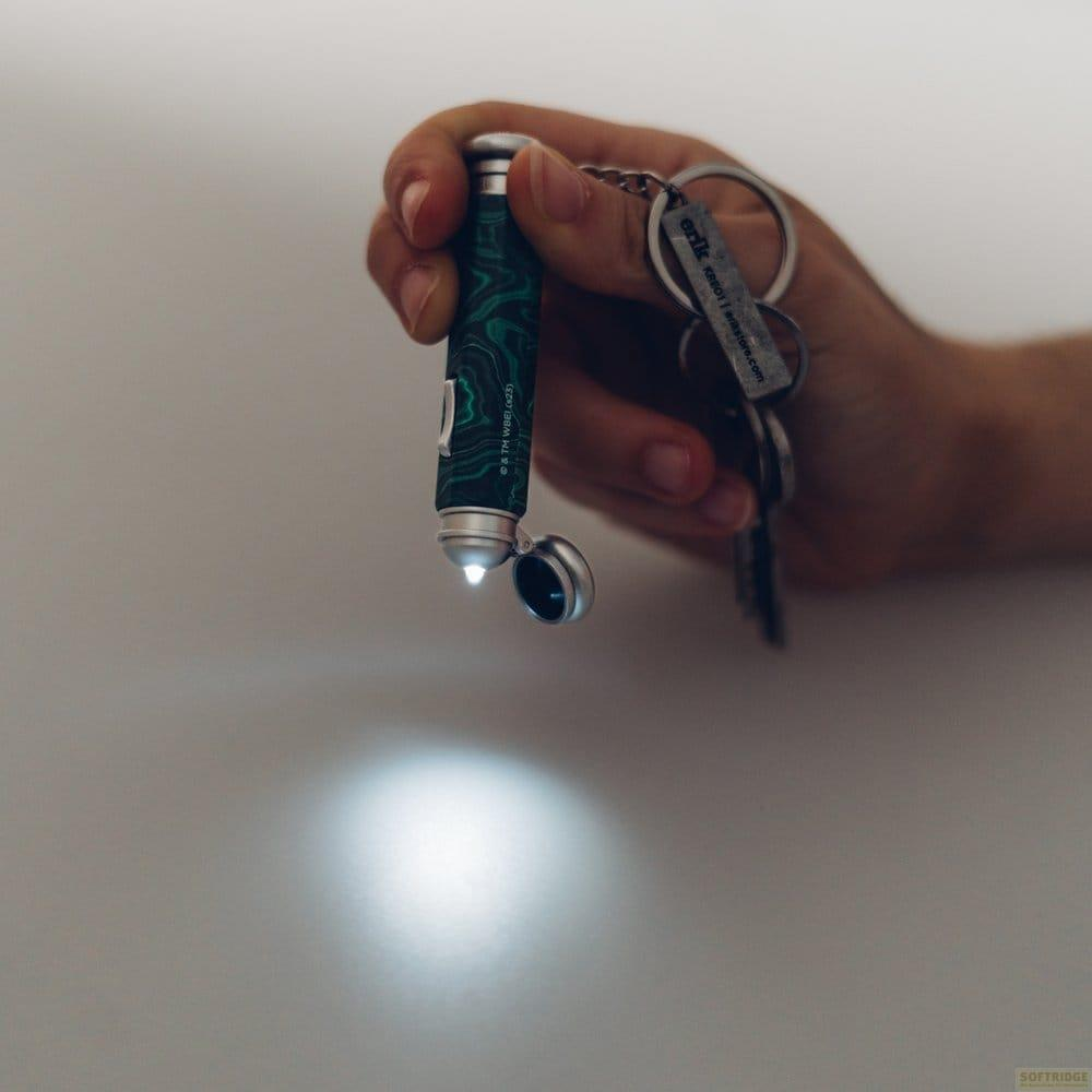Mano che tiene un portachiavi con mini torcia verde fantasia, che è accesa.