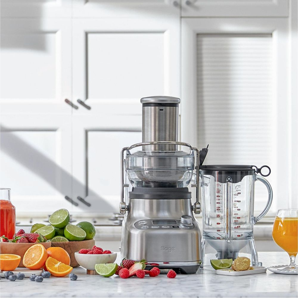 Un extracteur et un mixeur sur un plan de travail en marbre avec des fruits.