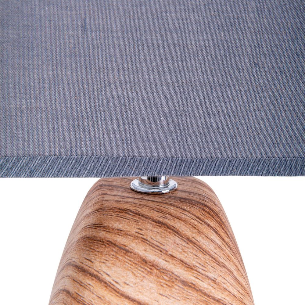 Ein Lampenschirm aus blauem Stoff über einem Holzsockel mit metallischem Detail.