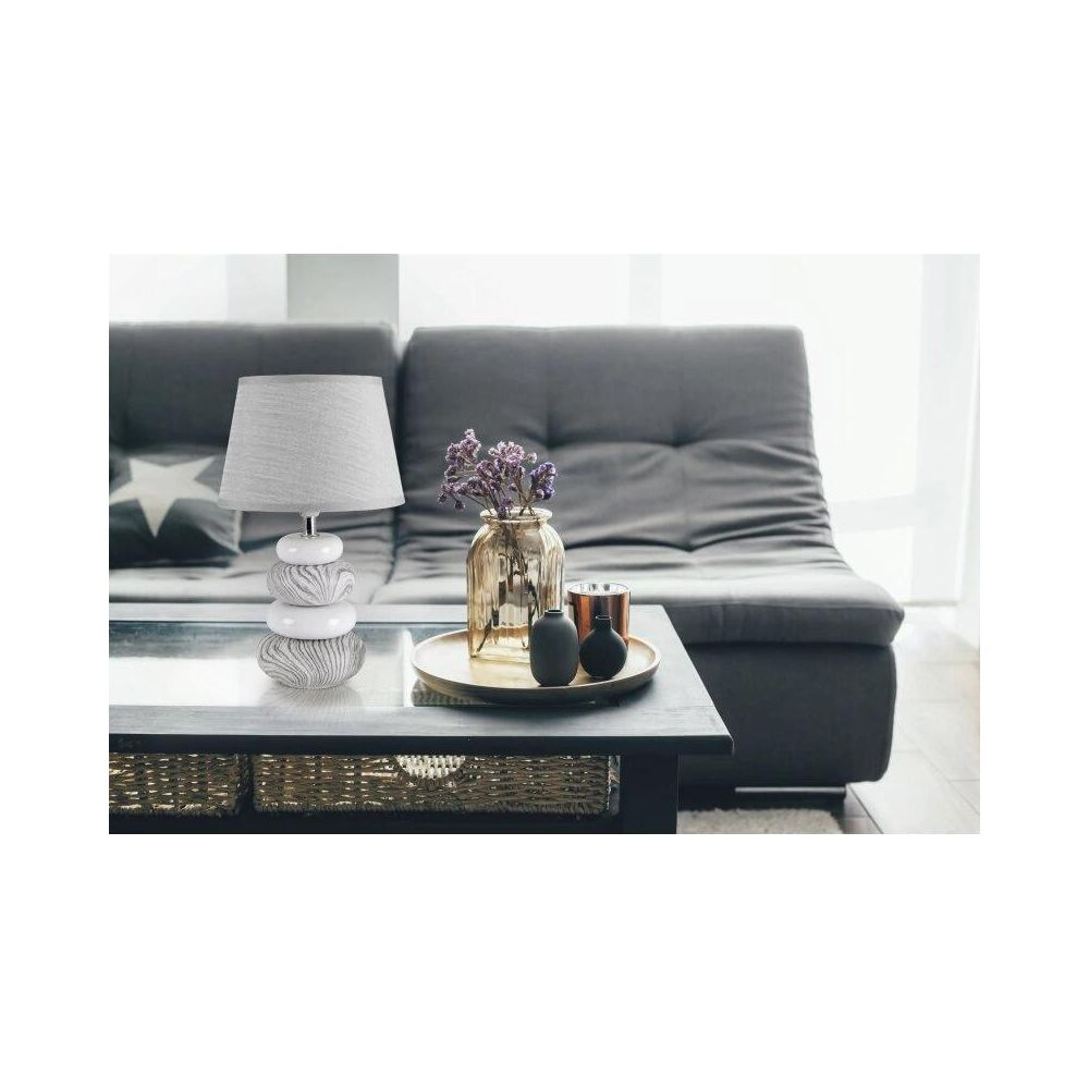 Ein Nachttisch mit Lampe, Vase mit Blumen und Kerzen auf einem Couchtisch vor einem Sofa.