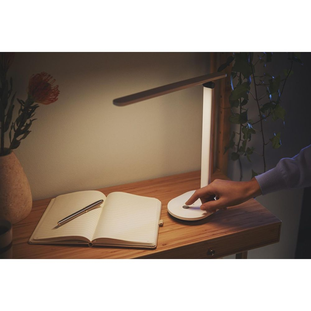 Una scrivania con una lampada, un taccuino e un vaso con fiori.