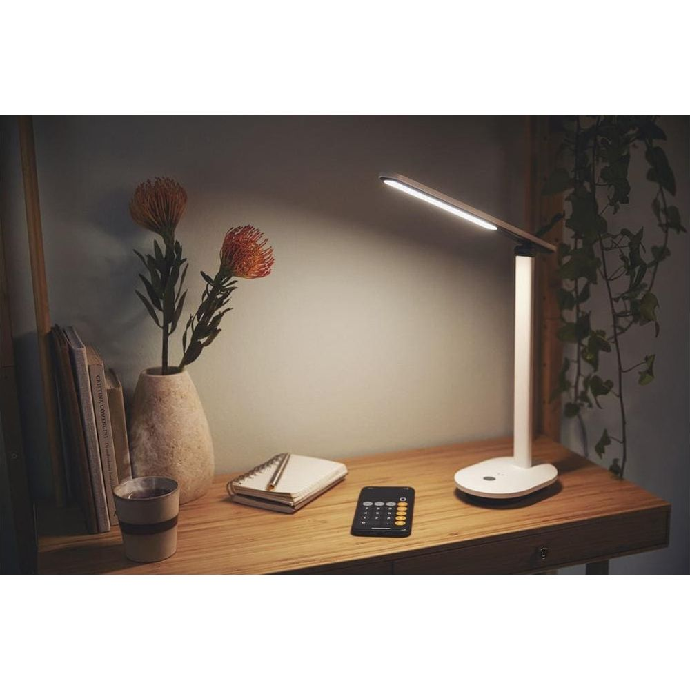 Una scrivania moderna con lampada, vaso di fiori, libri e taccuino.