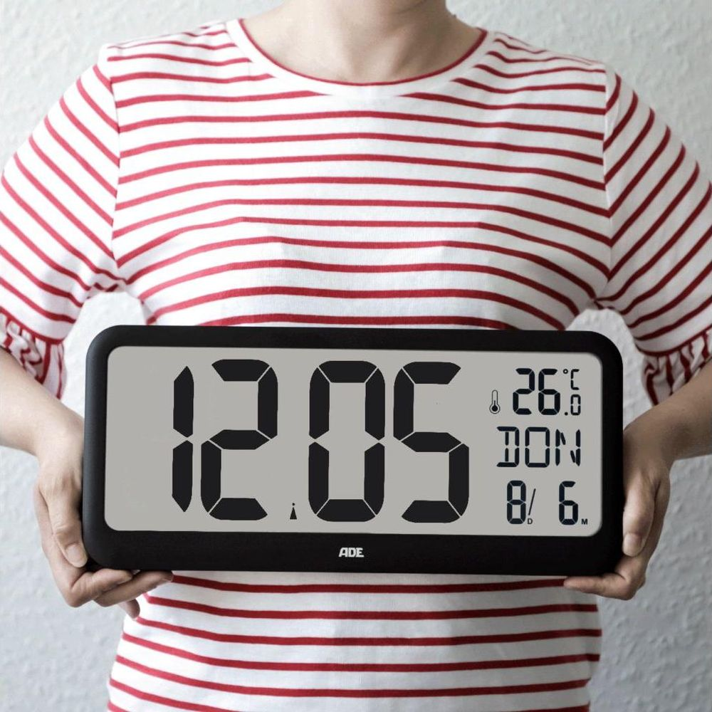 Person hält digitale Uhr mit Zeit 12:05, Temperatur 26°C, Tag DON, Datum 8/6.