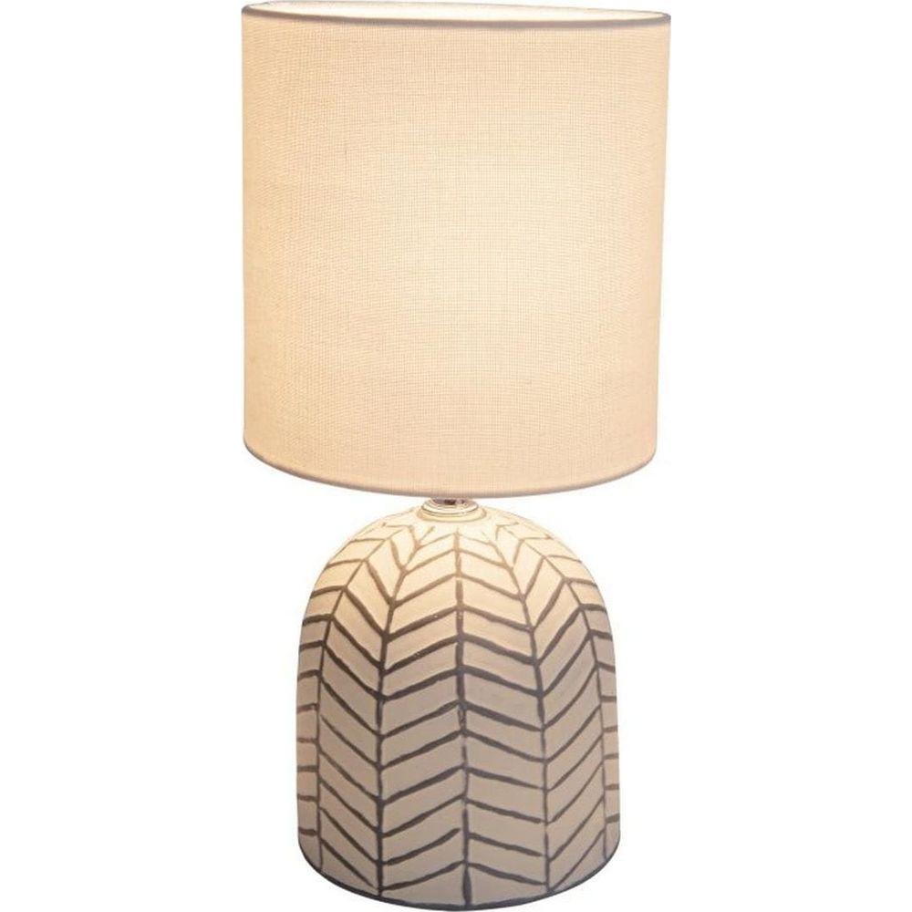 Eine Tischlampe mit einem weißen Lampenschirm und einem geometrisch gemusterten Sockel.