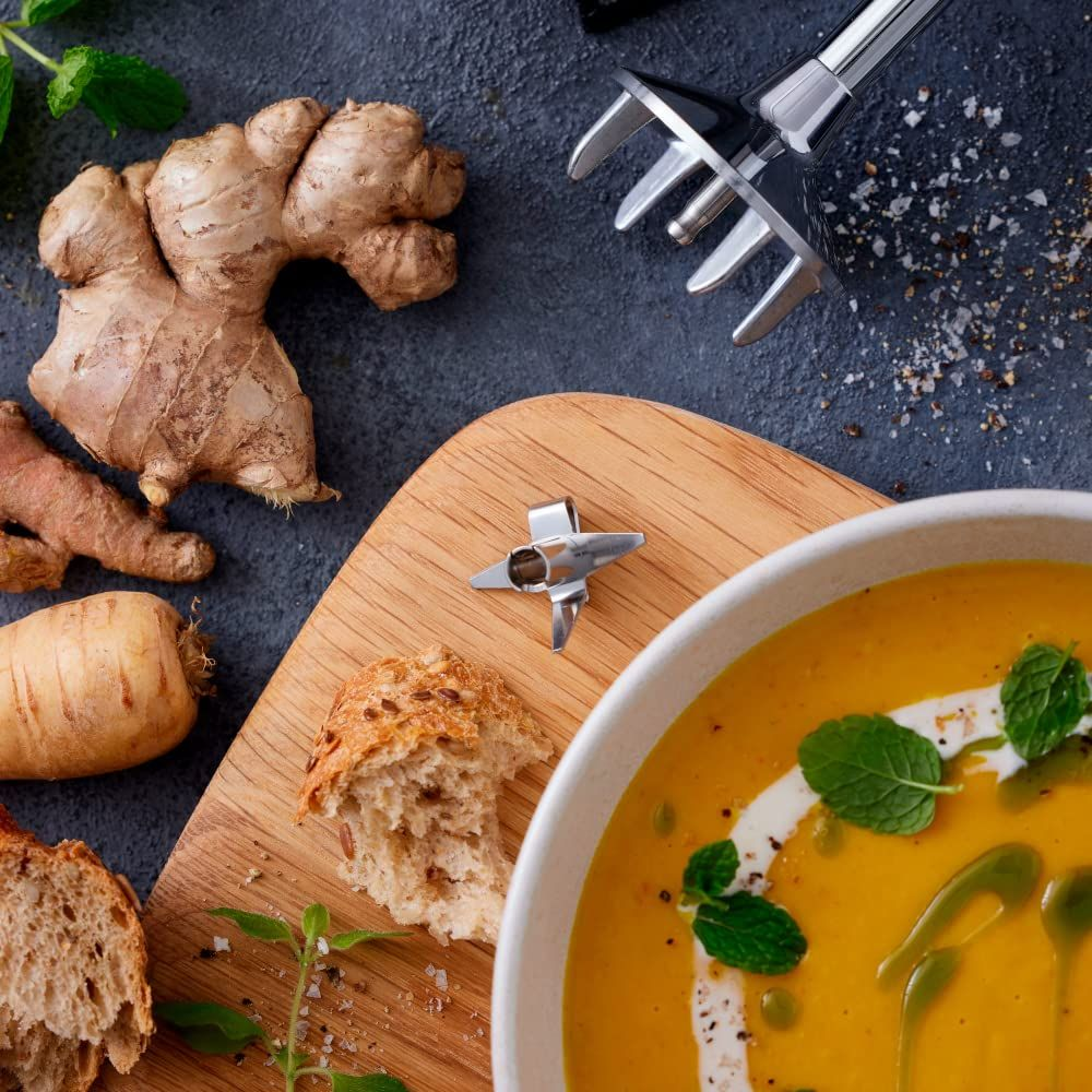 Una ciotola di zuppa di zucca con pane, zenzero e accessorio frullatore.