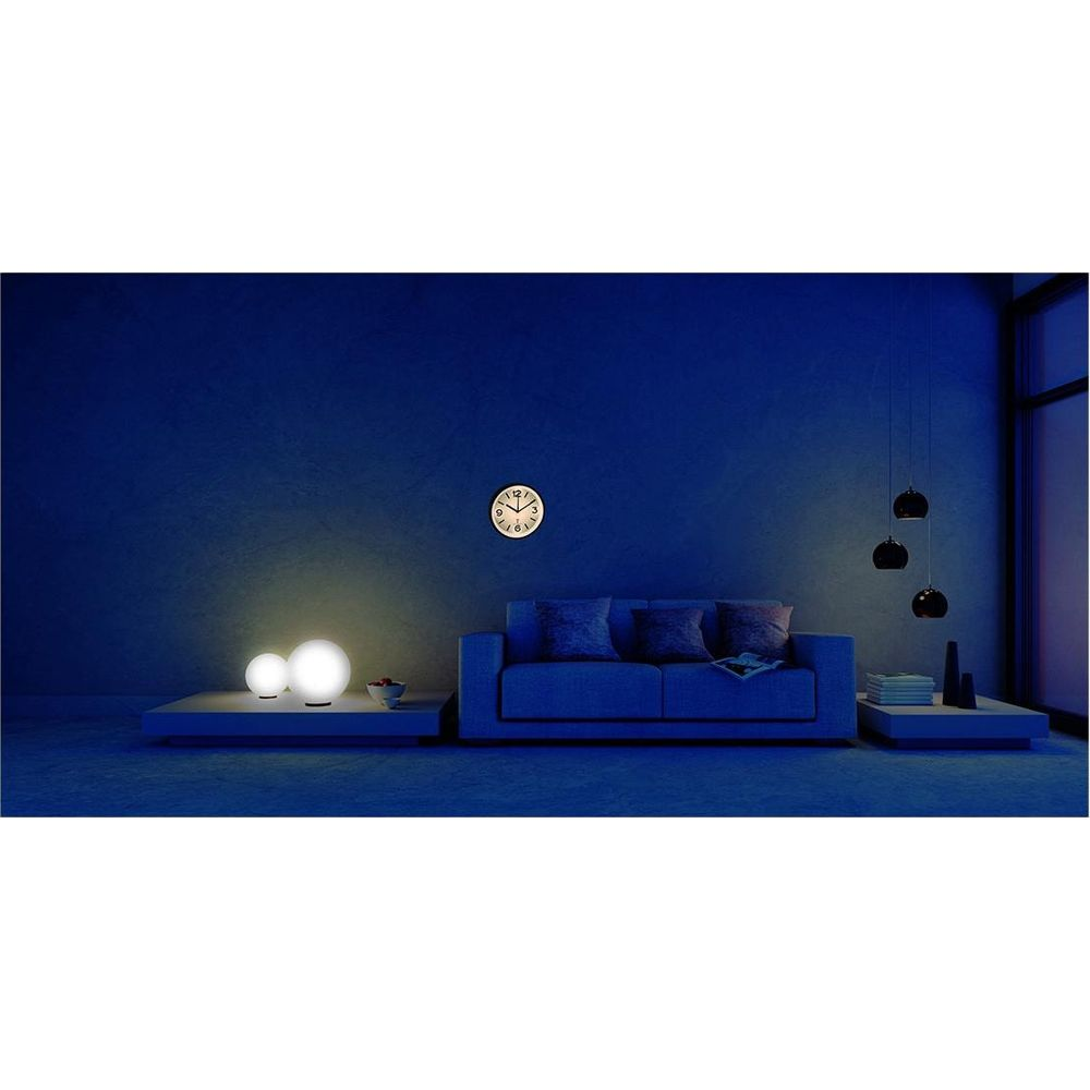 Ein Sofa steht vor einer blauen Wand mit einer Uhr. Zwei Lampen leuchten links.