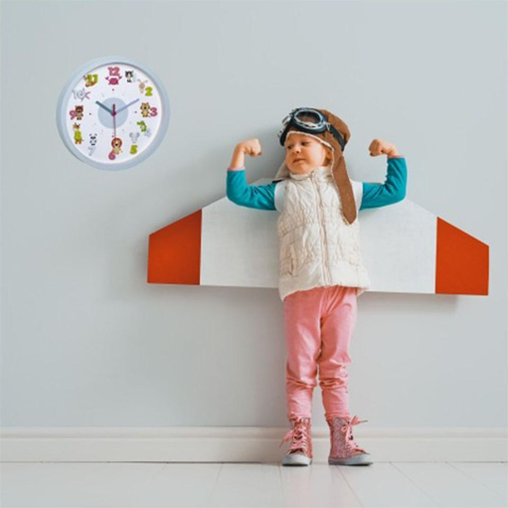 Kind als Pilot gekleidet, Arme anspannend; Uhr mit Zeichentricktieren an Wand.