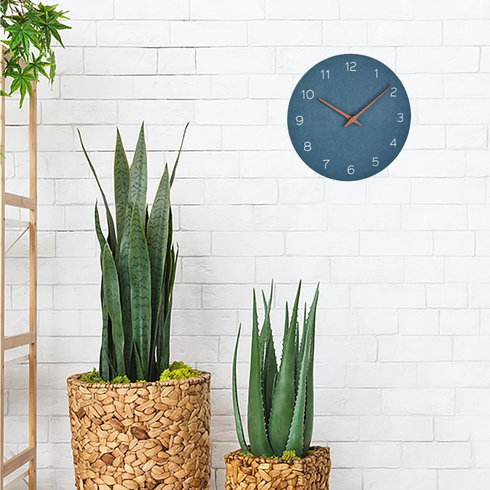 Ein blauer Wanduhr über zwei Topfpflanzen vor einer weißen Ziegelwand.