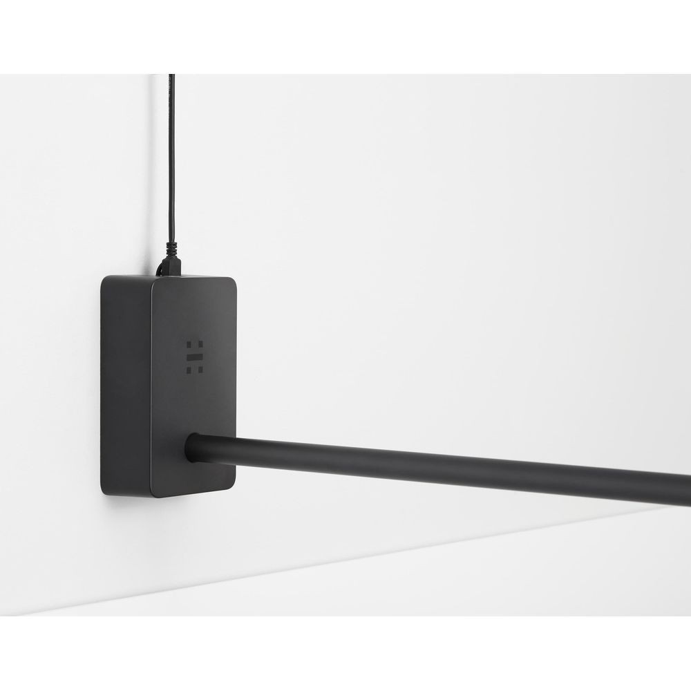 Ein schwarzes Rechteck mit Kabel und Stange hängt an einer weißen Wand.