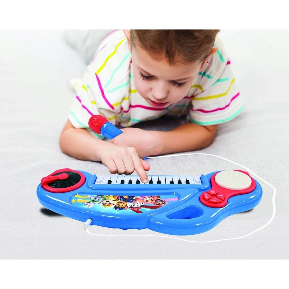 Chłopiec gra na niebieskiej zabawce-klawiaturze z mikrofonem. Na klawiaturze są postacie z Psiego Patrolu.