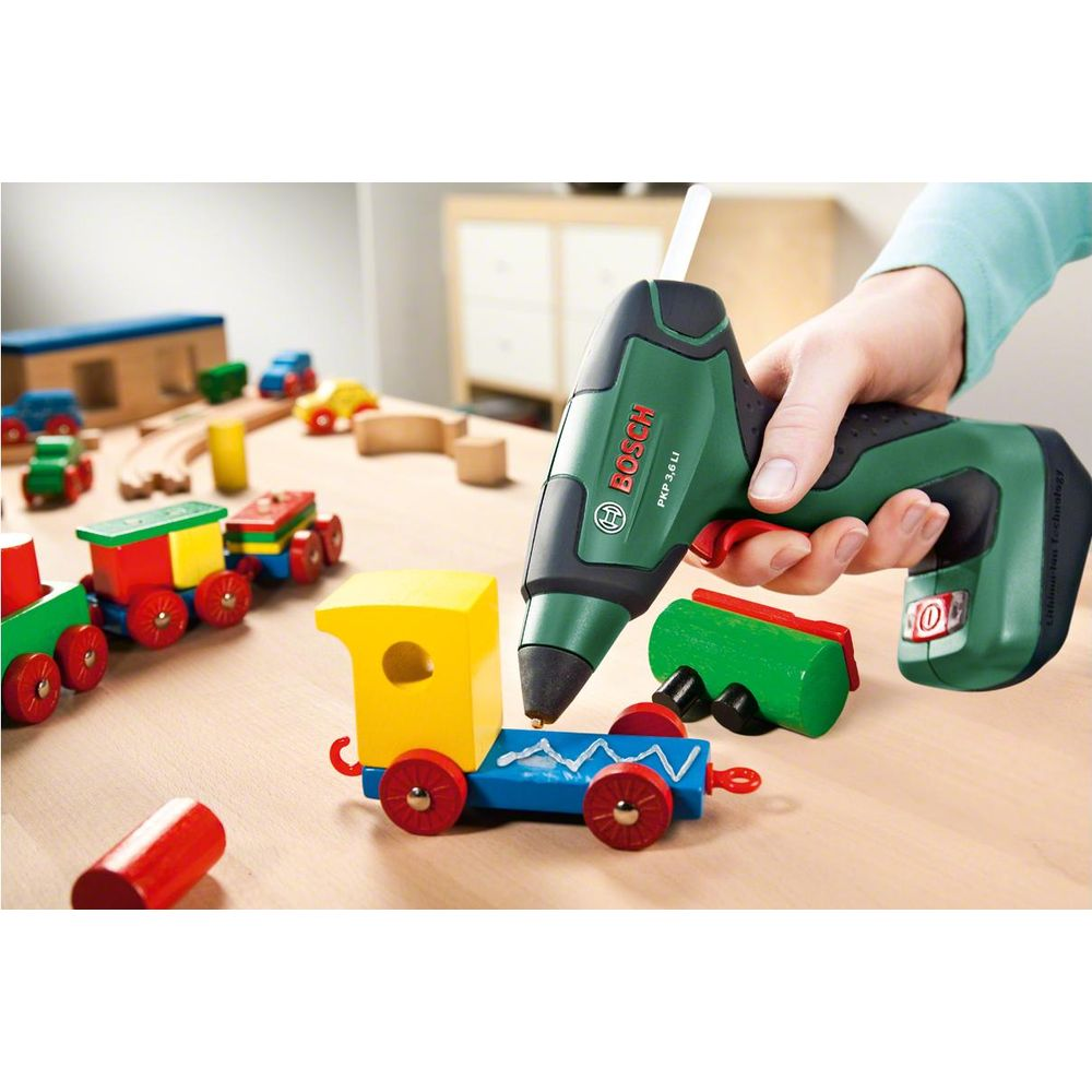 Zielony pistolet Bosch klei pociąg z drewna na drewnianym stole.
