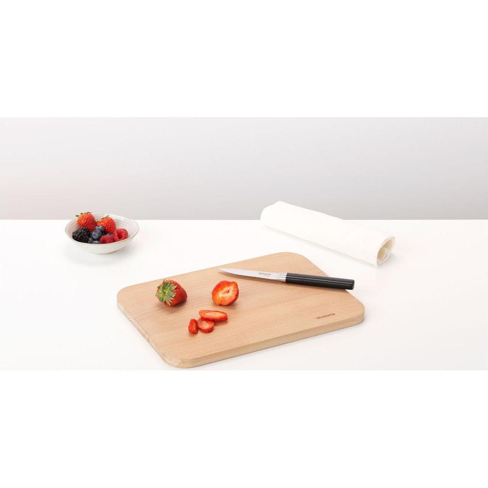 Ein Holzschneidebrett mit Erdbeeren, einem Messer und einer Schüssel Beeren.