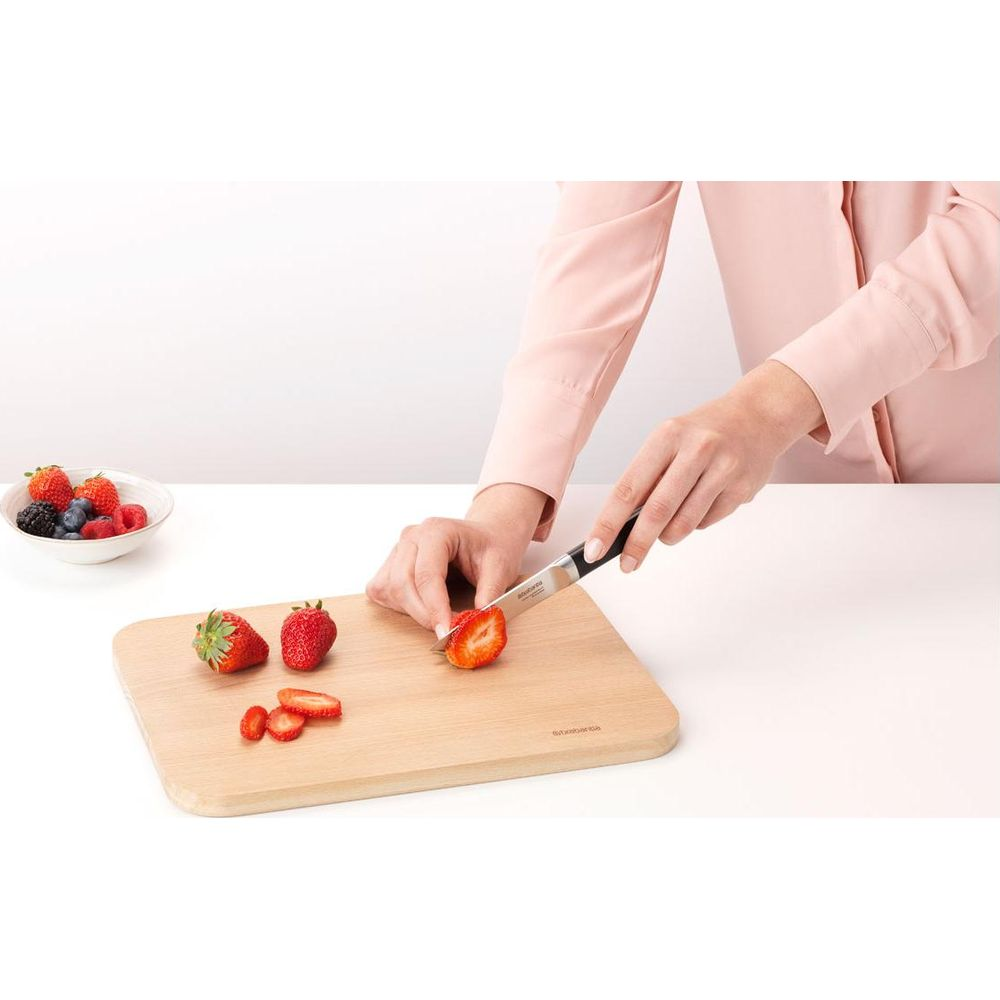 Eine Person schneidet Erdbeeren auf einem Holzbrett. Eine Schale mit Beeren steht links.