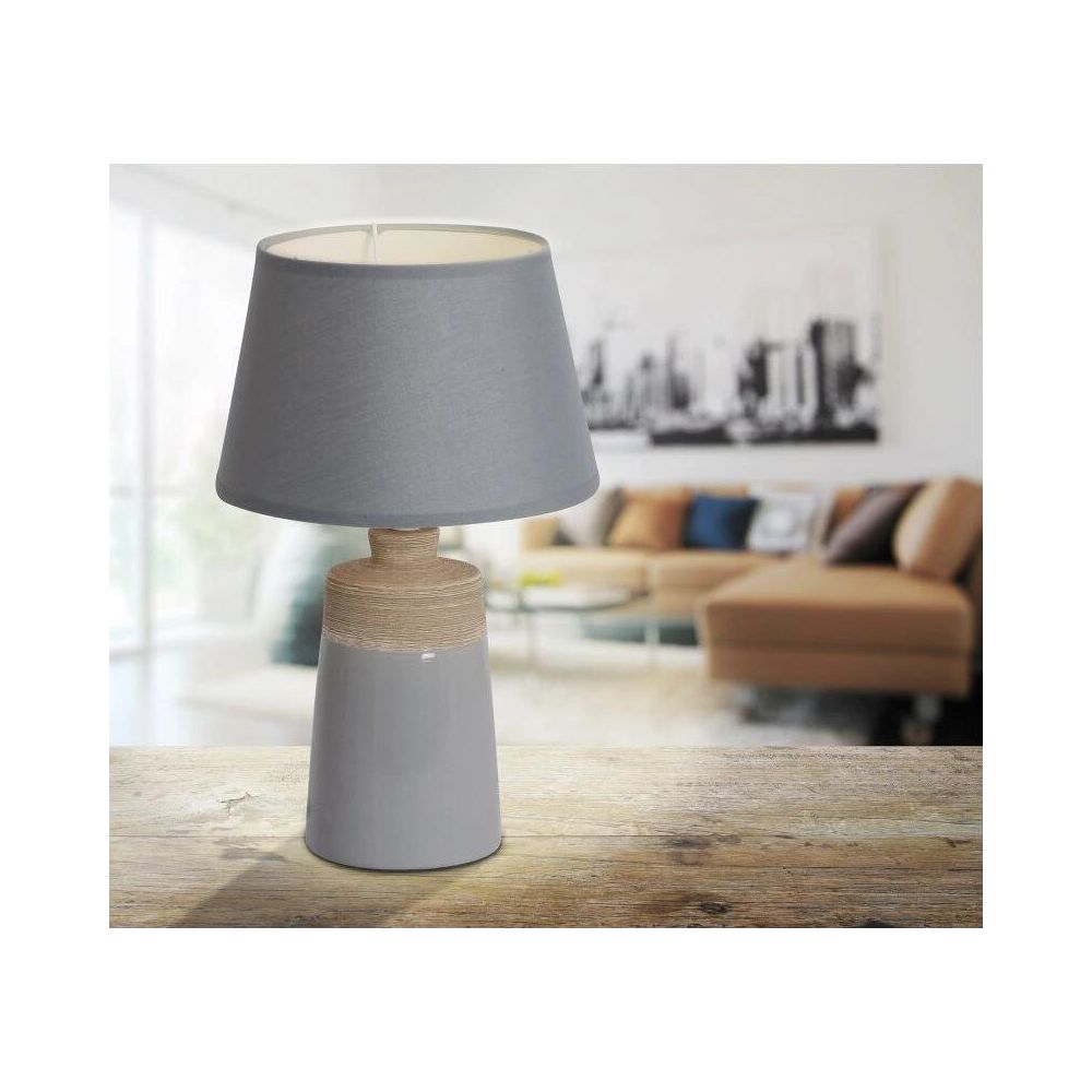 Graue Lampe mit Schnur-Detail auf Holztisch vor unscharfem Wohnzimmer.