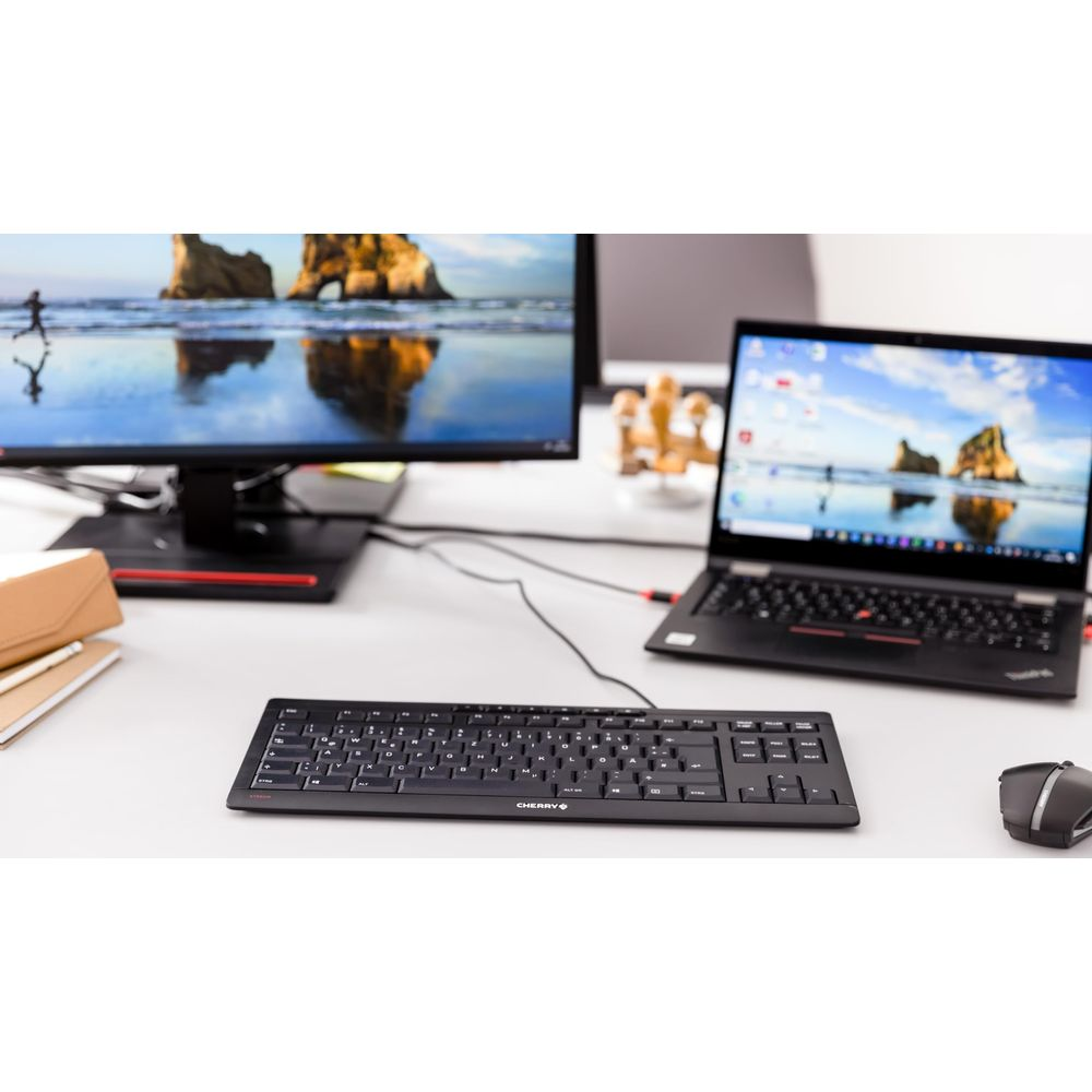 Ein Desktop-Setup mit Monitor, Laptop, Tastatur und Maus auf einem weißen Schreibtisch.