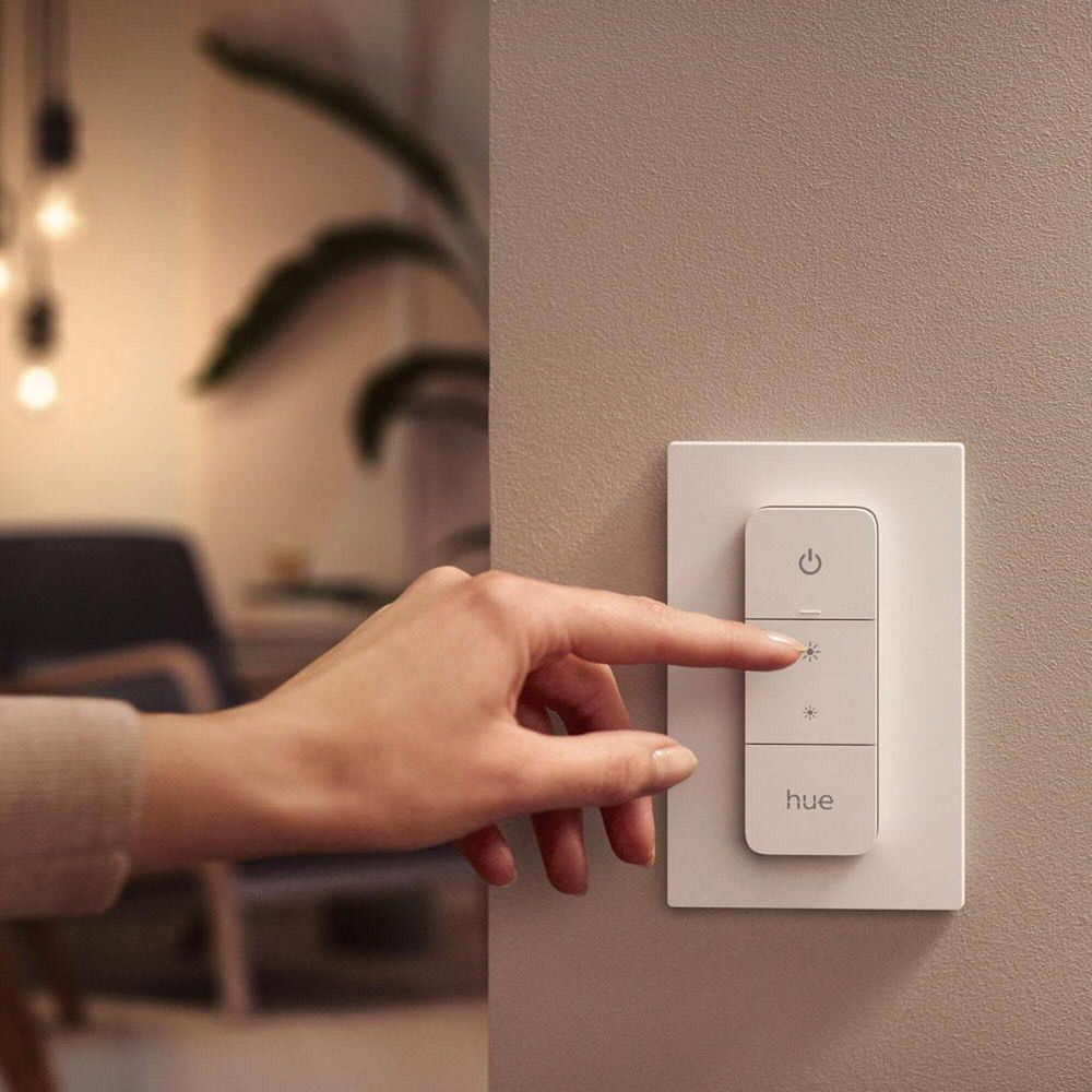 Una mano presiona un interruptor de luz con el logo de Hue. Al fondo se ve una habitación.