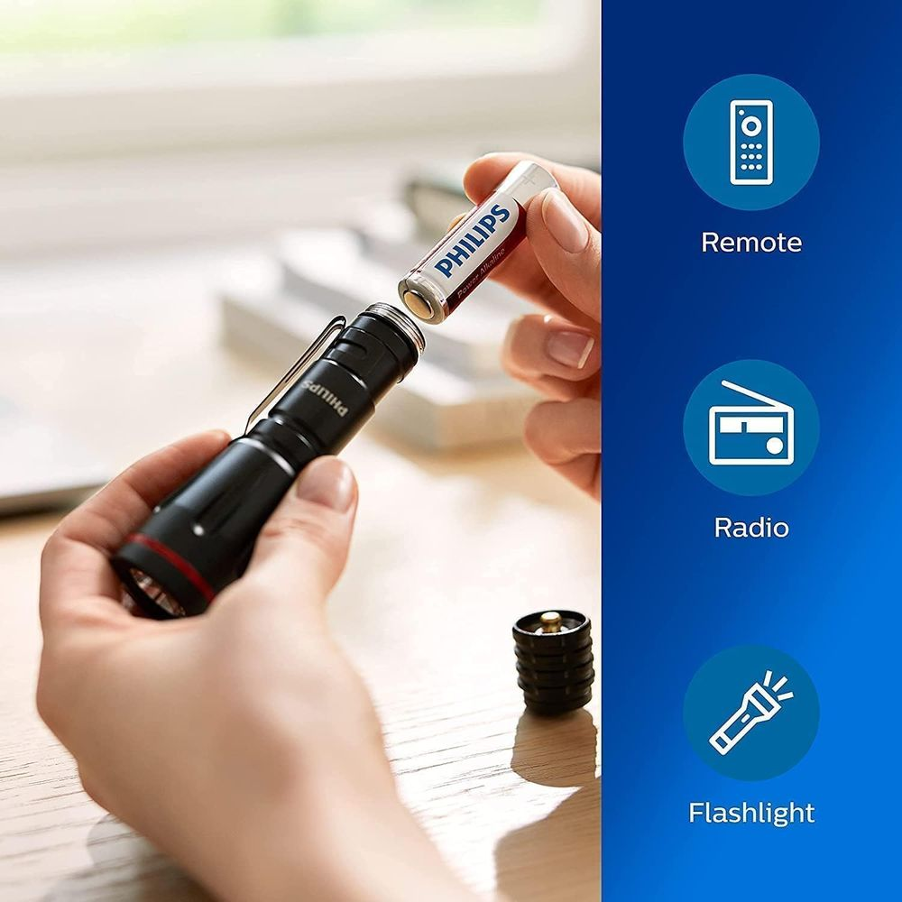 Ręka wkłada baterię Philips do czarnej latarki.