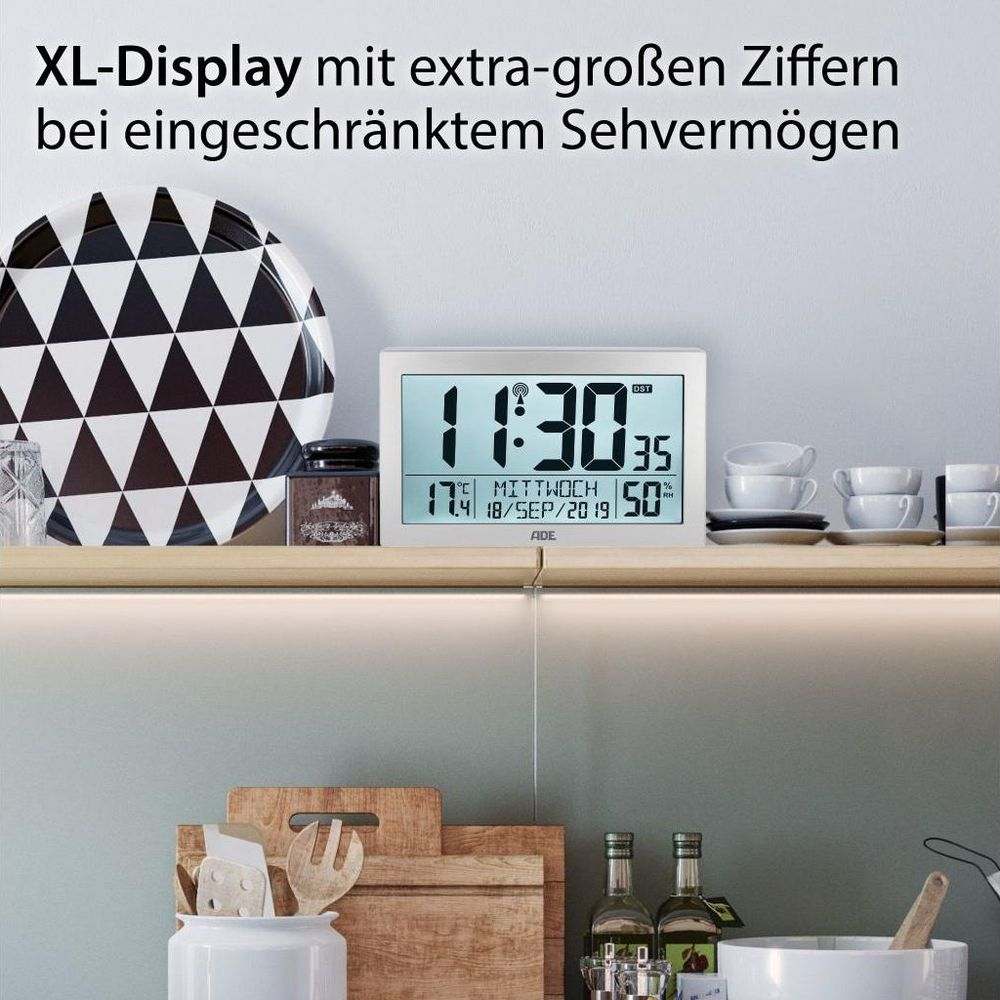 Digitaluhr mit Datum, Temperatur und Luftfeuchtigkeit auf einem Regal.