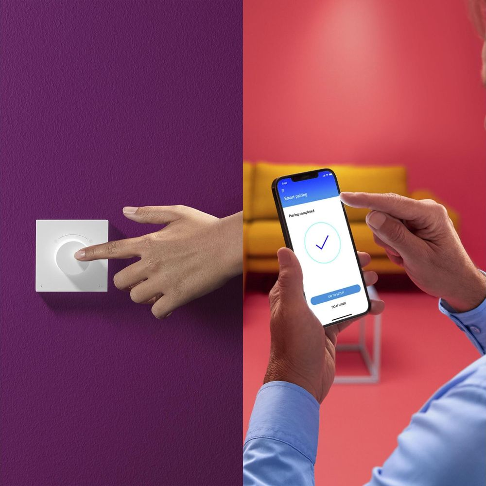 Een hand bedient een lichtschakelaar, een andere houdt een smartphone met koppeling voltooid.