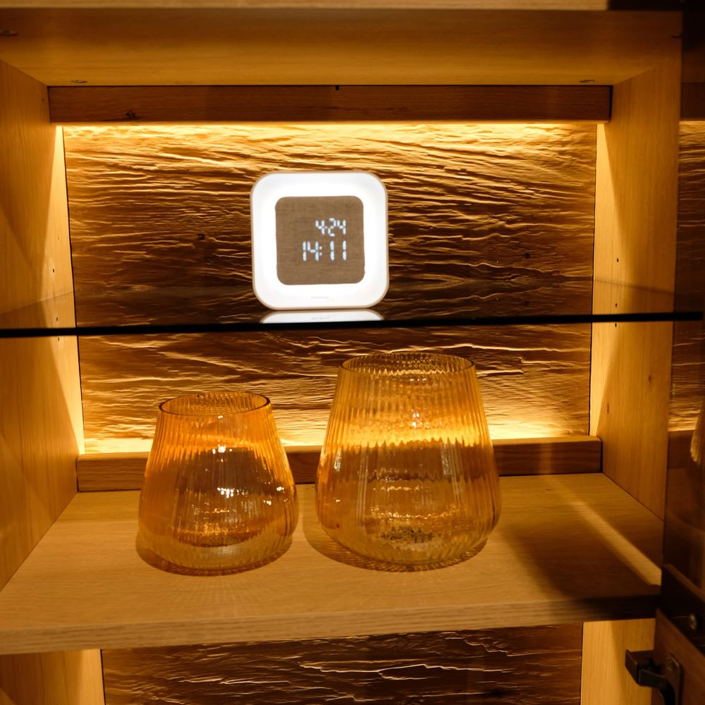 Un réveil numérique et deux verres ambre sur une étagère en bois éclairée.