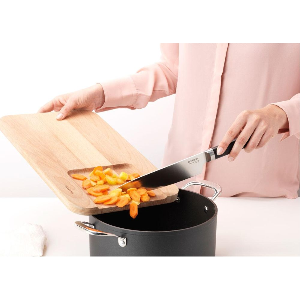 Gekochte Karotten werden von einem Holzbrett in einen Topf geschüttet.
