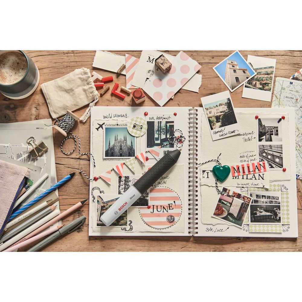 Ein Notizbuch mit Fotos, Stiften, Kaffee und Bastelmaterialien auf Holztisch.