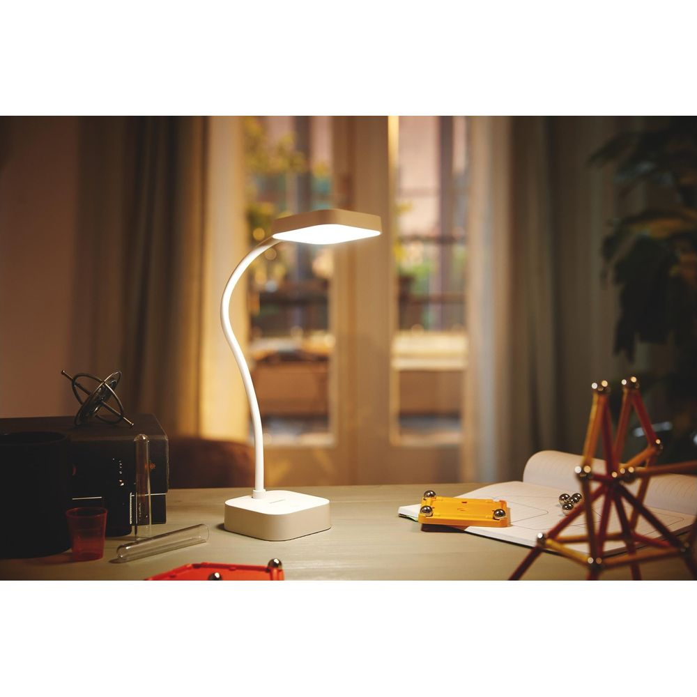Una lampada da scrivania bianca illumina un tavolo con materiali per hobby.