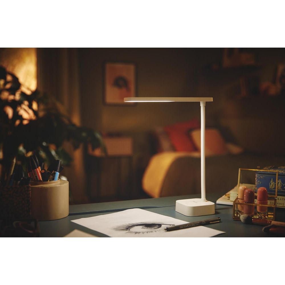 Eine weiße Schreibtischlampe beleuchtet eine Zeichnung eines Auges und Stifte.