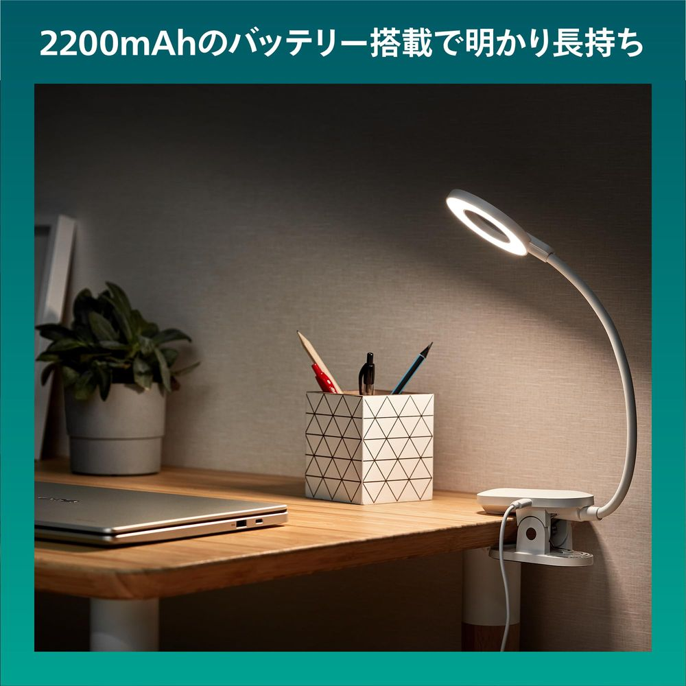 Una lámpara LED con pinza ilumina un escritorio con portátil, planta y portalápices.
