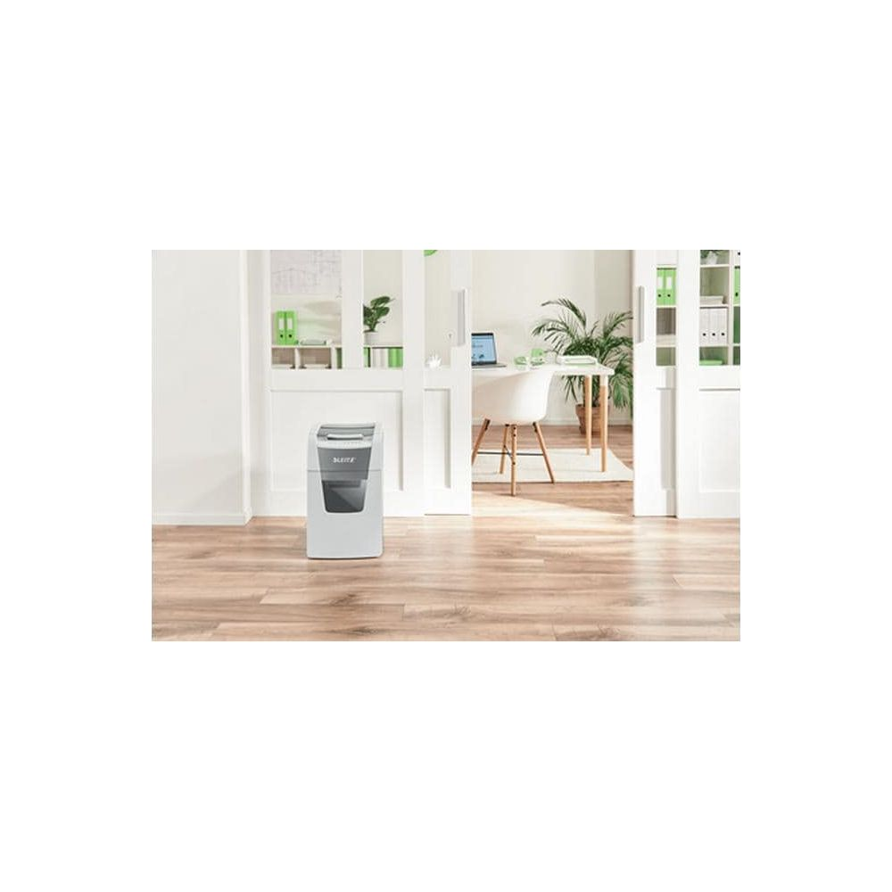 Une déchiqueteuse à papier blanche se trouve sur un parquet devant un bureau.