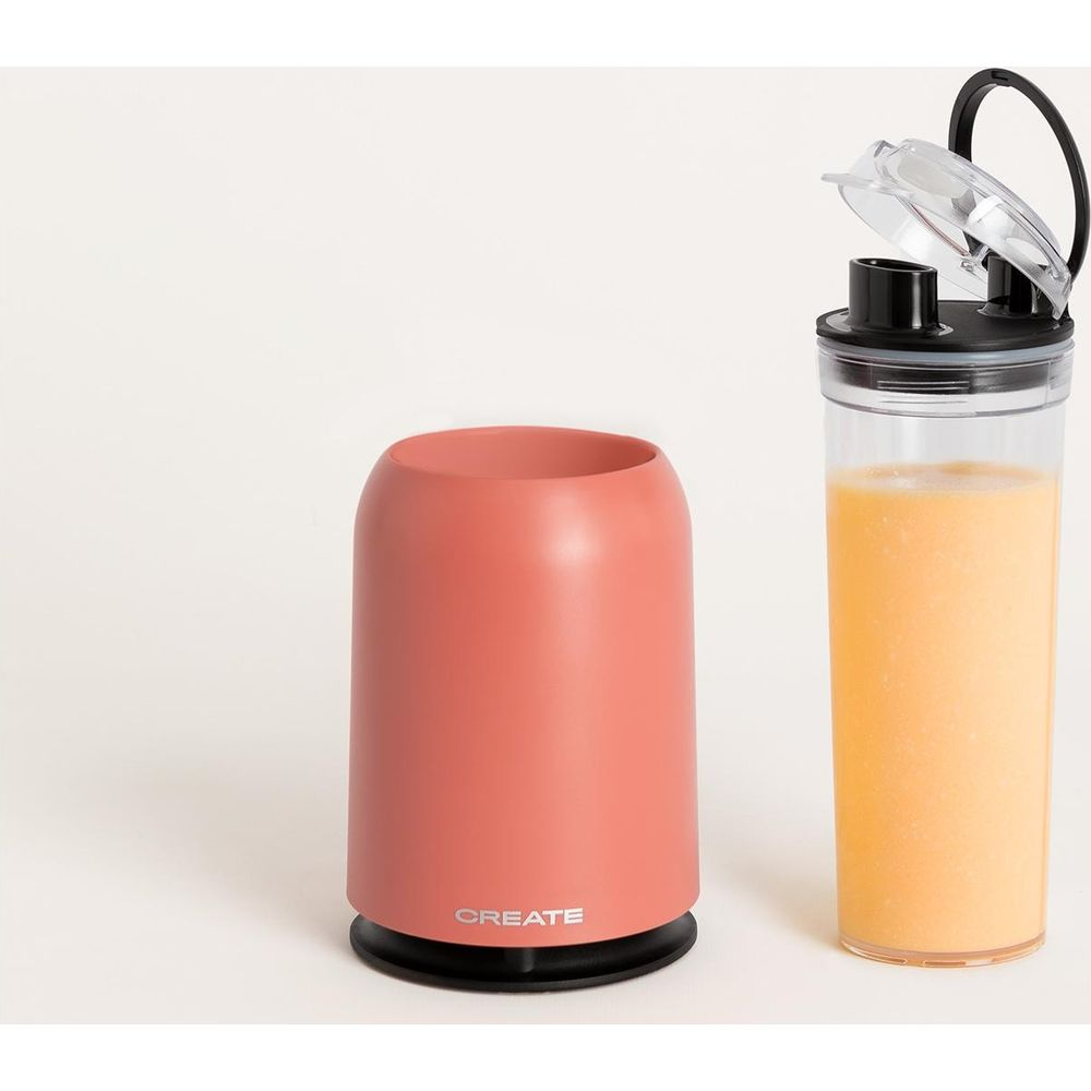 Un recipiente color coral junto a una taza de jugo de naranja.