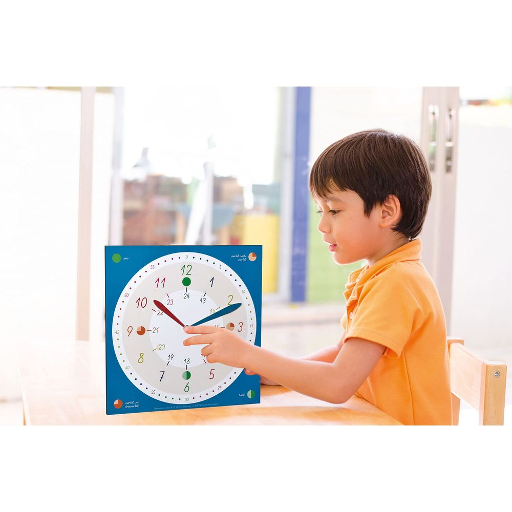 Ein Junge im orangefarbenen Hemd verstellt Zeiger auf einer blauen Uhr mit Zahlen und arabischem Text.