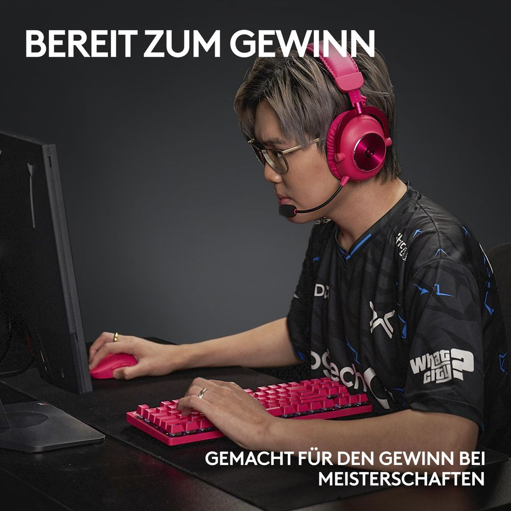 Gracz w różowych słuchawkach z mikrofonem gra na różowej klawiaturze i myszy.