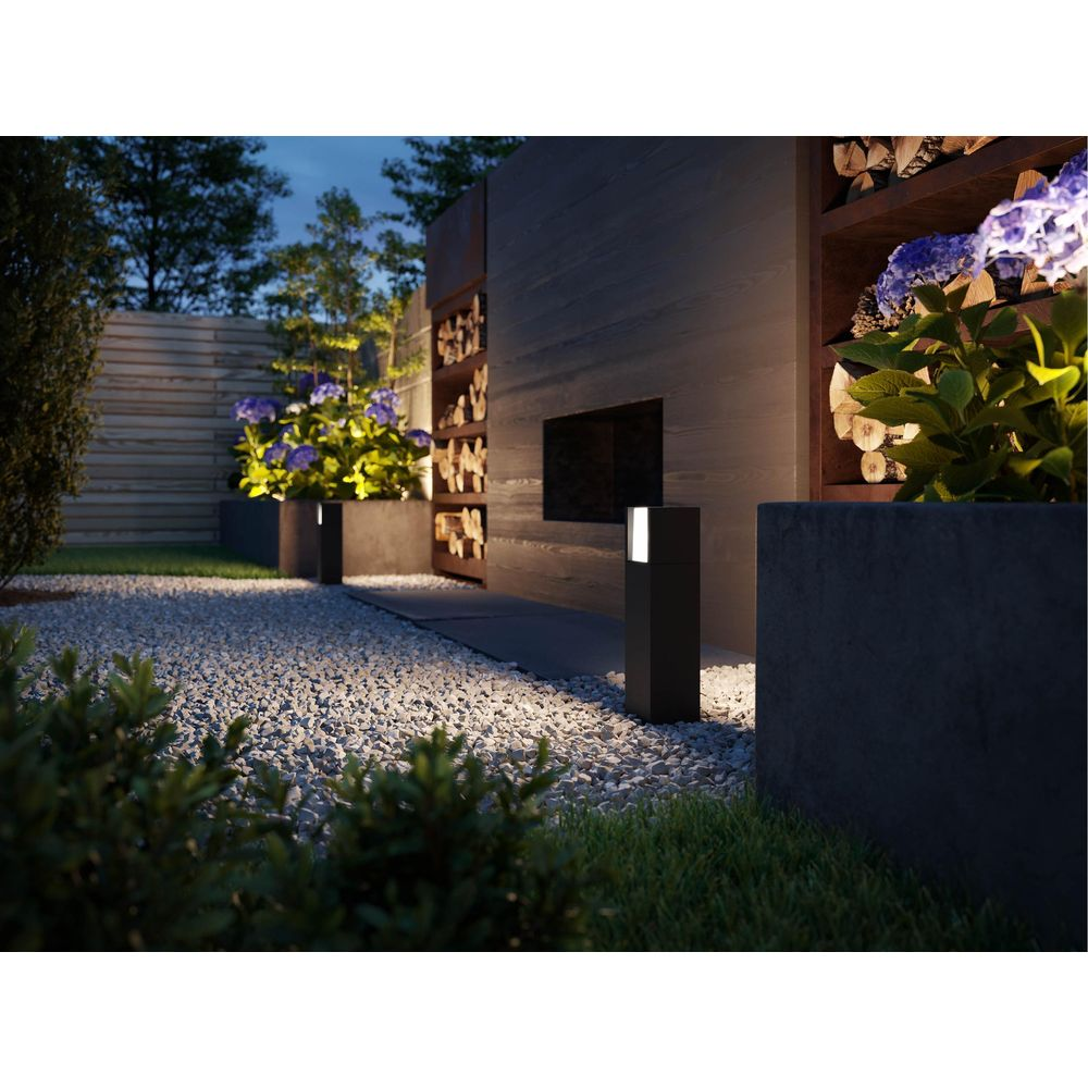 Un giardino moderno con sentieri di ghiaia, dissuasori illuminati e deposito legna.