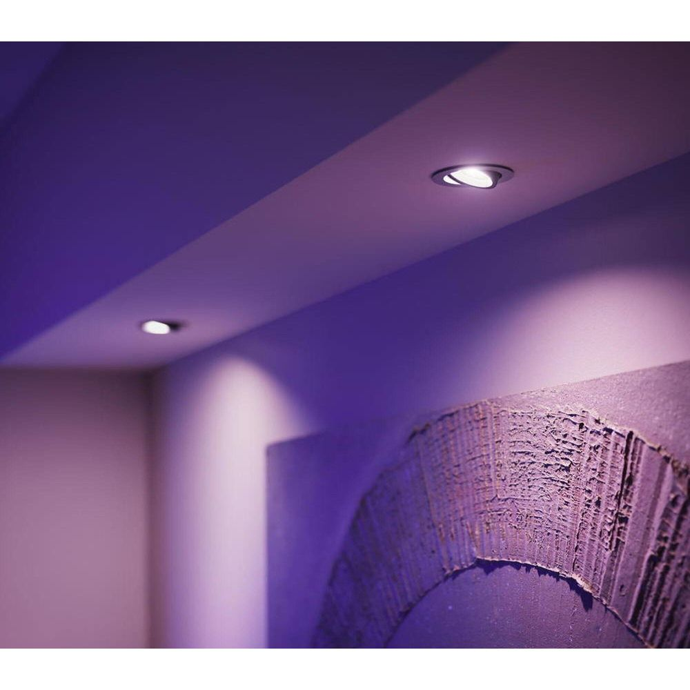 Focos empotrados iluminan un techo con luz púrpura. Una pared texturizada está al frente.