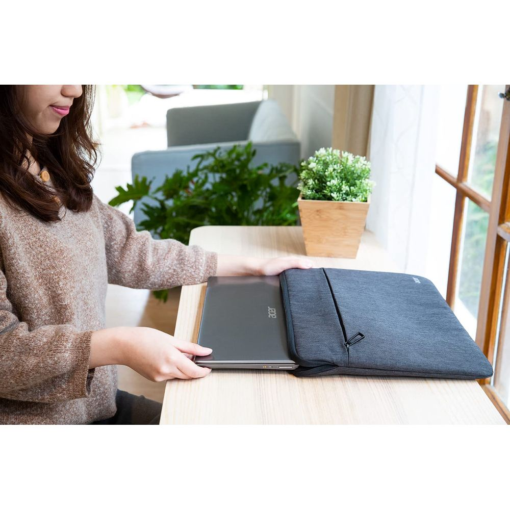Una donna fa scivolare un laptop in una custodia grigia su un tavolo di legno.