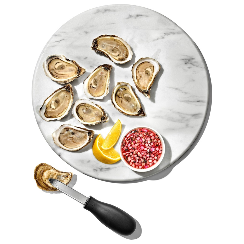 Frische Austern auf Marmorplatte mit Zitronenspalten und Mignonette-Sauce. Ein Austernmesser liegt daneben.